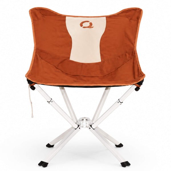 A folding camp chair in canyon orange fabric seat and backrest, featuring a cream-colored vertical panel on the backrest with a stylized orange letter CLIQ Q logo. The chair has a white metal folding frame with black plastic feet and leg caps, shown against a plain white background. Limited Edition MystiQ Canyon Orange - CLIQ